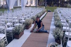 a woman sitting on the ground in front of rows of white chairs with flower arrangements