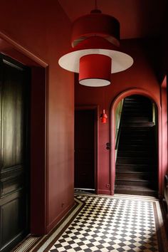 a hallway with red walls and black and white checkered flooring, two lamps hanging from the ceiling