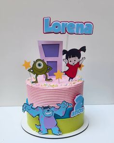 a pink and green birthday cake with cartoon characters on the top, sitting on a white table