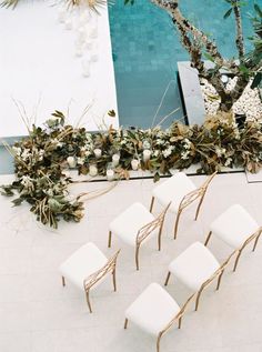 four white chairs sitting on top of a tiled floor next to a tree and pool