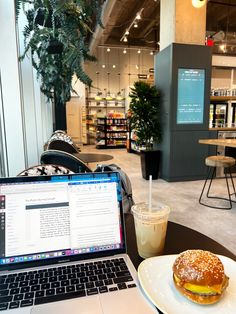 an open laptop computer sitting on top of a table next to a sandwich and drink