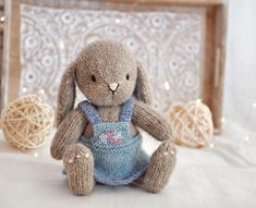 a knitted bunny sitting on top of a bed next to some balls of yarn