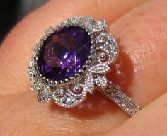 "A beautiful and intricate antique inspired filigree engagement ring featuring a velvety amethyst in a milgrain bezel. The center stone is a velvety purple amethyst, measuring about 9mm diameter (approximately 3 carats). It is set in an antique-inspired 14K white gold filigree ring, featuring 0.15 carats of GH VS2 diamonds. The ring is designed with an open gallery, allowing maximum light into the stone for best sparkle and making it easier to clean. The swirly gallery features two bezel-set \"s Filigree Engagement Ring Vintage, Purple Engagement Rings, Filigree Ring Gold, Open Gallery, Filigree Engagement Ring, Engagement Ring Vintage, Vs2 Diamond, Antique Inspiration, Gold Filigree