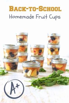 several jars filled with fruit sitting on top of a wooden table next to green leaves