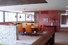 a dining room table with orange chairs next to a brick wall and windows in the background