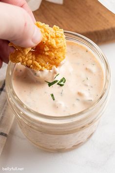 a person dipping some kind of food into a glass jar filled with dip and sauce