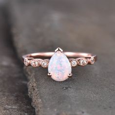 a white opal and diamond ring sitting on top of a rock