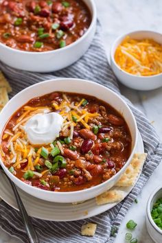 two bowls of chili with sour cream and tortilla crackers on the side