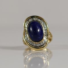 This vintage ring showcases an exquisite oval cabochon-cut lapis lazuli, set in rich yellow gold. The deep blue lapis is beautifully framed by a halo of sparkling diamonds, adding a touch of elegance and brilliance. The combination of the vivid lapis and the warm gold creates a striking contrast, making this ring a captivating piece. Perfect for those who appreciate timeless beauty and vintage charm, this ring is a true statement of sophistication. Size: 6 Metal Type: 14K(Tested) Weight: 9.0G Width: 23.74mm-3.13mm at shank Finger to Top of Ring: 13.8mm Gem Details:  Type: Lapis Lazuli Quantity: 1 Cut: Oval Cabochon Carat: Aprox 6.02 carats Dimensions: 14.2x10mm Color: Blue with Gold Flecks  Accent Gems: Type: Diamonds Quantity: 19 Shape: Round Brilliant Cut Carat Weight: 0.20cttw We look f Luxury Cabochon Lapis Lazuli Rings, Luxury Elegant Cabochon Sapphire Ring, Luxury Cabochon Sapphire Ring Elegant Style, Gold Flecks, Blue Lapis, Vintage Ring, Oval Cabochon, Sparkle Diamonds, Bezel Setting