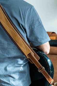 a man with a blue shirt is holding a brown leather guitar case in his right hand