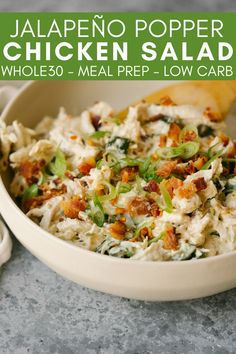 a white bowl filled with chicken salad next to a wooden spoon on top of a table