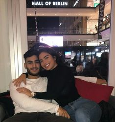 a man and woman sitting on a red couch in front of a mall of berlin sign