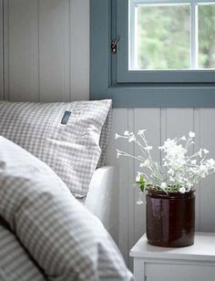 a vase with flowers sitting on top of a white table next to a pillow and window