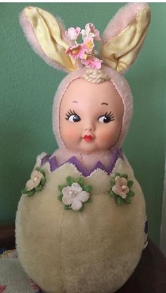 an old fashioned doll is sitting in a basket with flowers on it's head