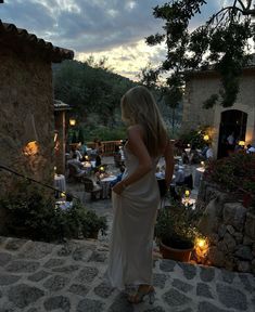 a woman in a white dress is standing outside at dusk with candles lit on the ground