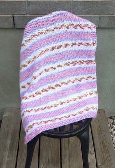 a pink and white knitted blanket sitting on top of a wooden chair next to a brick wall