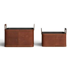 two brown leather storage bins with handles on each side and one holding a black cushion