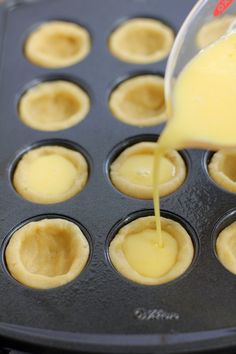 someone pouring sauce on top of some cupcakes in a muffin tin filled with them