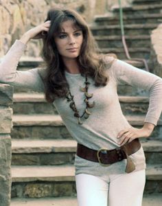 a woman with long hair and a necklace on her neck is leaning against a stone wall