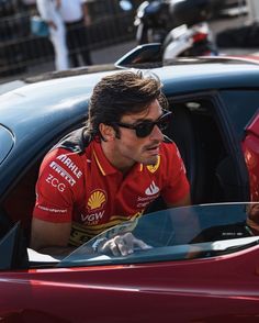 a man sitting in the drivers seat of a red sports car with sunglasses on his head