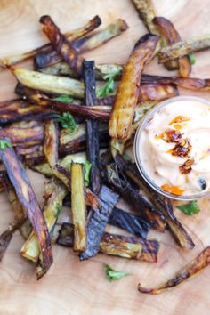 some french fries are on a cutting board with a small bowl of dip in the middle