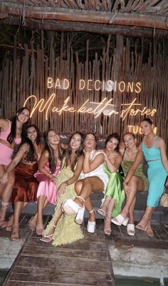 a group of women sitting next to each other in front of a bamboo wall with neon lights