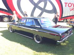 an old black car parked in front of a large red and white sign with people standing next to it