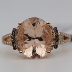 an oval shaped peach morganite surrounded by brown and white diamonds on a gold band