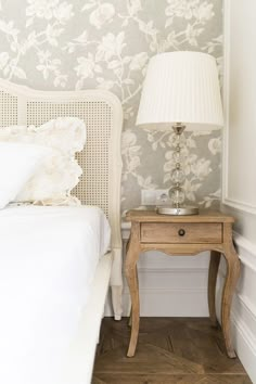 a white bed sitting next to a nightstand with a lamp on top of it