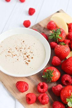 a bowl of yogurt next to some strawberries and apples on a cutting board