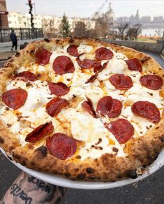 a large pepperoni and cheese pizza on a white platter in front of a man's arm