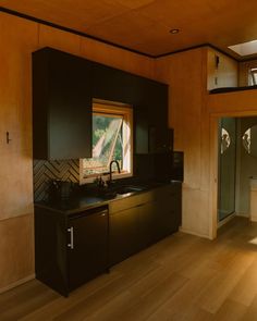 an empty kitchen with wood floors and black cabinetry on the wall, along with a large window