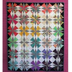 a colorful quilt hanging on the wall in front of a pink frame with black and white stripes