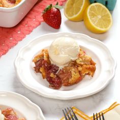 a white plate topped with fruit cobbler next to a bowl of ice cream and strawberries