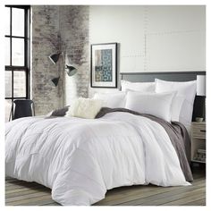 the comforter is white and grey in this bedroom with brick wall, windows, and wooden flooring