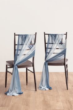 two chairs with blue drapes on them sitting in front of a white wall and wooden floor