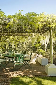 an outdoor dining area with green chairs and tables under a pergolated arbor covered in moss