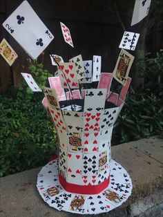 a hat made out of playing cards on top of a cement slab with trees in the background