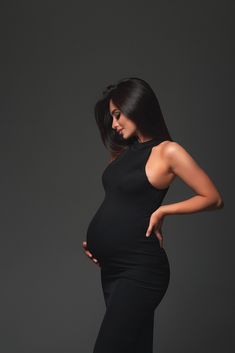 a pregnant woman in a black dress poses for the camera with her hands on her hips