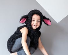 a young child dressed in a black sheep costume sitting on the floor with his legs crossed