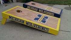 two michigan wolverines cornhole boards sitting on the side of a sidewalk in front of a house