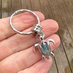 a hand holding a silver turtle shaped keychain