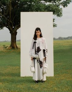 a woman standing in front of a large white piece of art on the grass near a tree