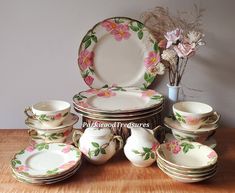 a table topped with lots of white and pink dishes next to a vase filled with flowers