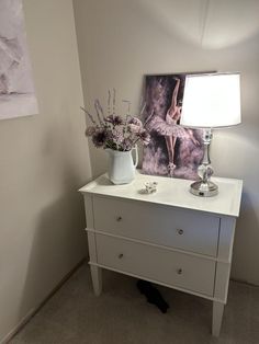 a white dresser with flowers and a lamp on top