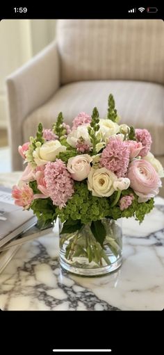 a vase filled with pink and white flowers on top of a marble table next to a couch