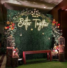 a green wall with flowers and birds in cages next to a bench that says better together