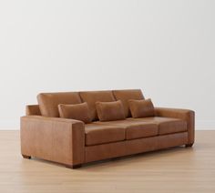 a brown leather couch sitting on top of a hard wood floor next to a white wall