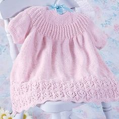 a pink knitted dress sitting on top of a doll's chair next to flowers