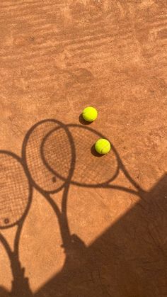 two tennis rackets and three yellow balls on the clay court, with shadow from one person's hand